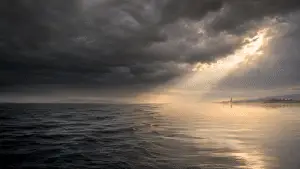 dawn light breaking through storm clouds over calm water symbolizing peace after anxiety and worry